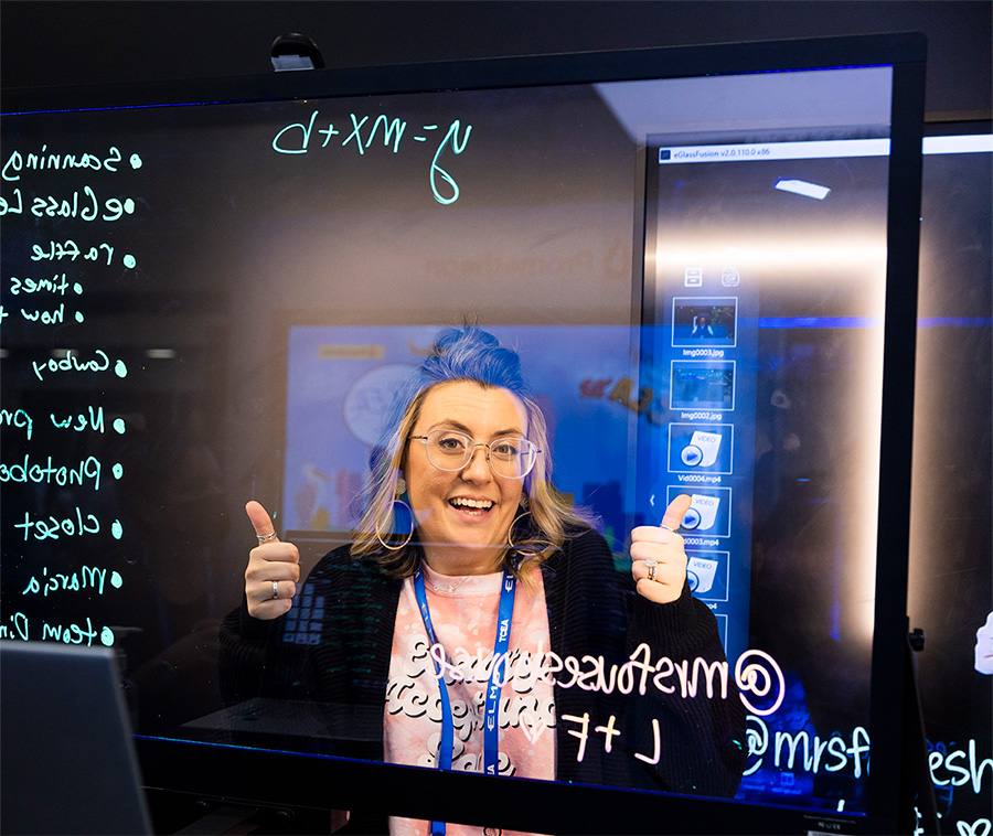 Teacher giving thumbs up sign behind glass display technology.