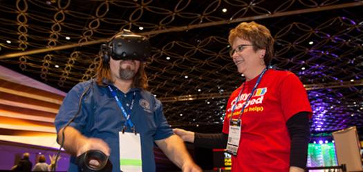 Convention volunteer helping an attendee wearing a virtual reality headset.